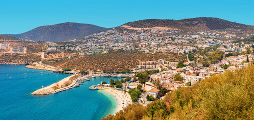 Majestic aerial panoramic view of the seaside resort town Kalkan in Turkey. Romantic lighthouse at entrance to the marina and hotels and villas with orange roofs waiting for tourists