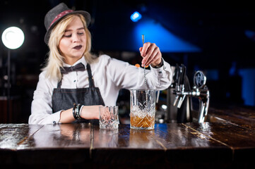 Expert woman barkeeper formulates a cocktail behind the bar
