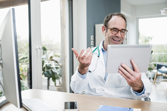Happy doctor with digital tablet gesturing on video call at hospital