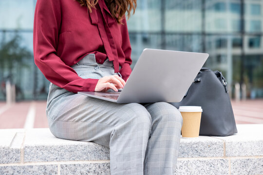 Businesswoman using laptop sitting on bench at office park