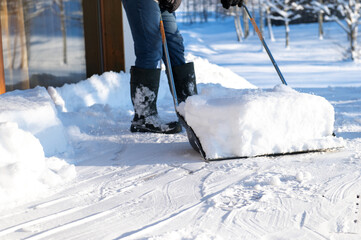 a man in rubber boots with a snow shovel cleans the snow from the terrace of the house