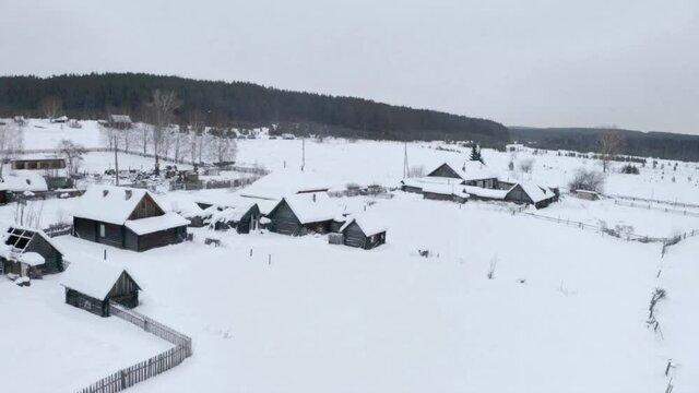 Snowy bird's-eye view. Clip. A white village in the snow with small wooden houses and next to it a large forest with tall trees