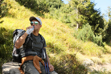 Fototapeta na wymiar Tired hiker drinking water outdoors on sunny day