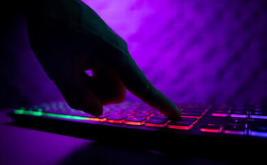 Hands on a glowing keyboard on a colored abstract background. The gamer plays the keyboard. Close-up.