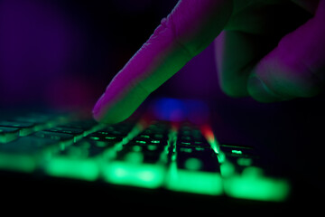 Hands on a glowing keyboard on a colored abstract background. The gamer plays the keyboard. Close-up.