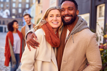 Multi Cultural Couple With Friends Walking Along Residential City Street In Fall Or Winter