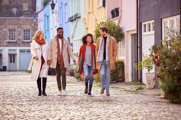 Multi Cultural Couple With Friends Walking Along Residential City Street In Fall Or Winter