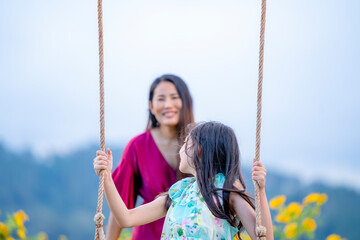 Happy daughter enjoying summer day at a playground over yellow flowers mountain.