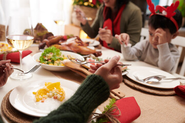 Hands of woman eating delicious salad at Christmas dinner with her family
