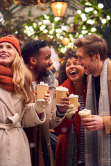 Group Of Friends Drinking Hot Chocolate With Marshmallows In Snow At Outdoor Christmas Market