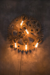 Steampunk architectural style design element of interior.Lamp bulbs fixed on iron industrial gear cogwheels sprocket lighting illuminated equipment