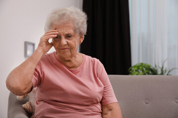 Senior woman with headache sitting on sofa at home. Space for text
