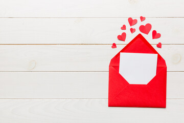 Red paper envelope with empty white card and heart on colored background. top view valentines day...
