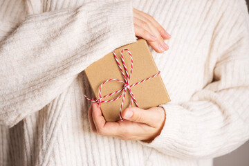 Woman in cozy beige knitted sweater giving christmas craft gift boxes with red ribbon. Giving presents concept.Valentine day and mother's day gift concept.