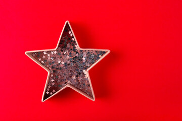  Star shaped box with confetti on a red background top view. Festive Christmas and new year background