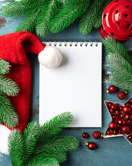 Christmas or New Year's blue festive background with an open blank notebook, fir branches and red decorations. A checklist or a letter to Santa. Top view with copy space	