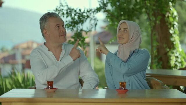 A young woman in hijab and her husband spend time in a cafe.The young couple is pointing to the middle of the screen with their fingers. Creative people can put whatever they want where shown.