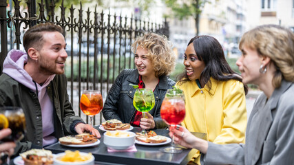 Multiracial happy young people eating and drinking, diverse cheerful mates laughing enjoying meal, having fun sitting together at restaurant table