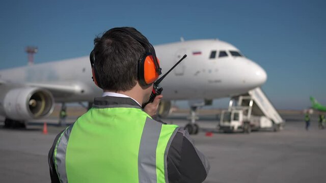 Airport. Aircraft engineer man worker mechanic controlling work airdrome. Man supervisor in headphones checking airplane safety flight, Plane airplane on background. Travel traffic control concept