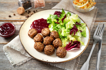 Swedish meatballs with salad and lingonberry jam in a bowl closeup. Traditional Scandinavian dish in a ceramic plate on a light gray wooden culinary background