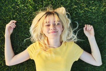 Top view of a beautiful teenage blonde lying on the green grass.