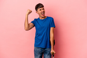 Young mixed race man with crutches isolated on pink background raising fist after a victory, winner...