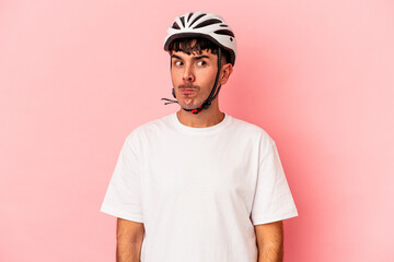 Young mixed race man wearing a helmet bike isolated on pink background confused, feels doubtful and unsure.