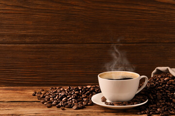 Cup of aromatic hot coffee and beans on wooden table, space for text