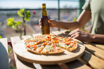 Close-up of pizza and beer bottle on table. Male hand holding bottle over table with pizza slices....