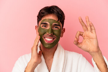 Young mixed race man wearing beauty facial mask isolated on pink background