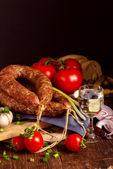 Appetizing smoked homemade sausage and vodka. Herbs, fresh tomatoes, canned cucumbers and garlic on background