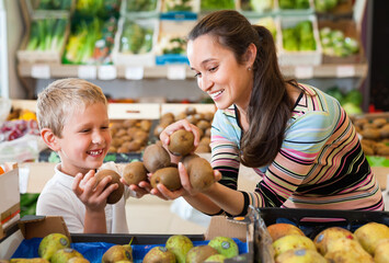 Fototapeta premium Portrait of happy positive smiling woman and her little son choosing kiwi at shop