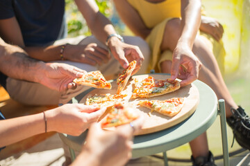 Close-up of pizza on round table. Pizza slices on plate. Male hands and female taking pieces. Party, friendship, food concept
