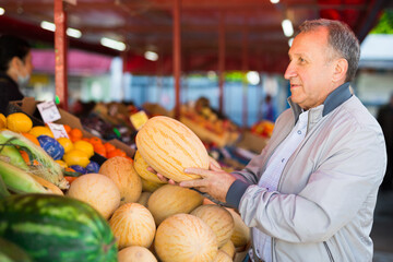 Man choosing melons in fruit shop