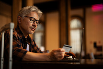 Businessman working on laptop and sitting in cafe. Senior man holding credit card.