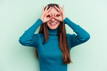 Young caucasian woman isolated on green background showing okay sign over eyes