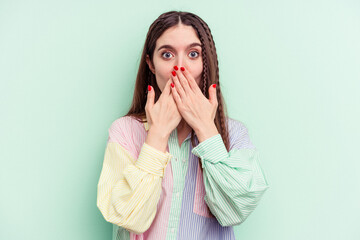 Young caucasian woman isolated on green background shocked covering mouth with hands.