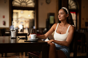 Stylish young woman drinking coffee at cafe. Beautiful girl enjoy in fresh coffee..