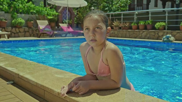 Little girl in pink swimsuit swimming in pool and smiling at camera.A little girl is having fun in the pool.