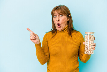 Middle age caucasian woman holding chickpea jar isolated on blue background pointing to the side