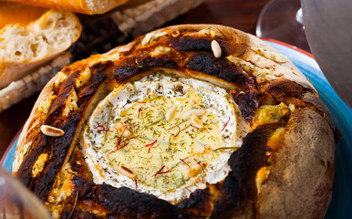 Delicious French fondue from camembert cheese melted in bread bowl with pine nuts and spices..