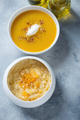 White bowls with millet porridge and pumpkin soup, elevated view on a light-blue stone background, vertical shot