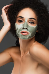 sensual african american woman with naked shoulders and clay mask on face looking at camera isolated on grey