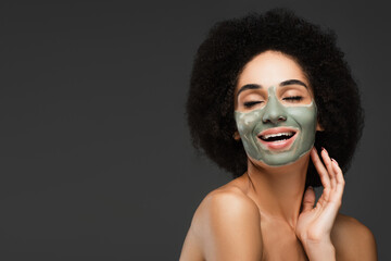 happy african american woman with clay mask on face smiling with closed eyes isolated on grey