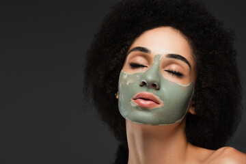 young african american woman with closed eyes pampering face with clay mask isolated on grey