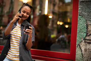 Fototapeta premium Happy girl enjoying in sunny weather and fresh coffee. Gorgeous casual brunette talking to the phone