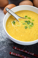 Close-up of egg-drop soup topped with scallions in a white bowl, vertical shot on a dark-grey stone background