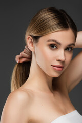 Fototapeta premium pretty young woman with perfect skin holding hair while looking at camera isolated on grey
