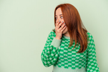 Young caucasian woman isolated on green background thoughtful looking to a copy space covering mouth with hand.