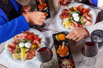 Due persone sedute ad un tavolo di un ristorante mentre mangiano l'antipasto accompagnato da due calici di vino rosso - obrazy, fototapety, plakaty